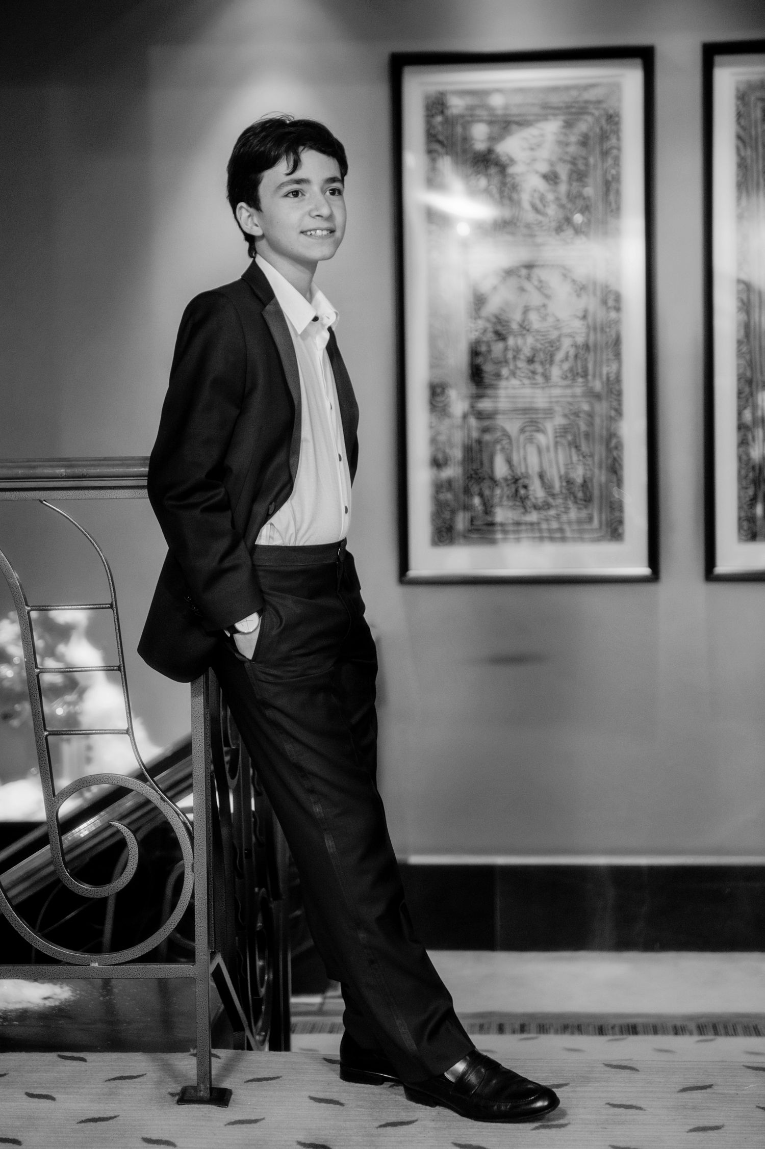 A black and white photo series shows someone in a formal suit posing with a chair against a wall with framed artwork.