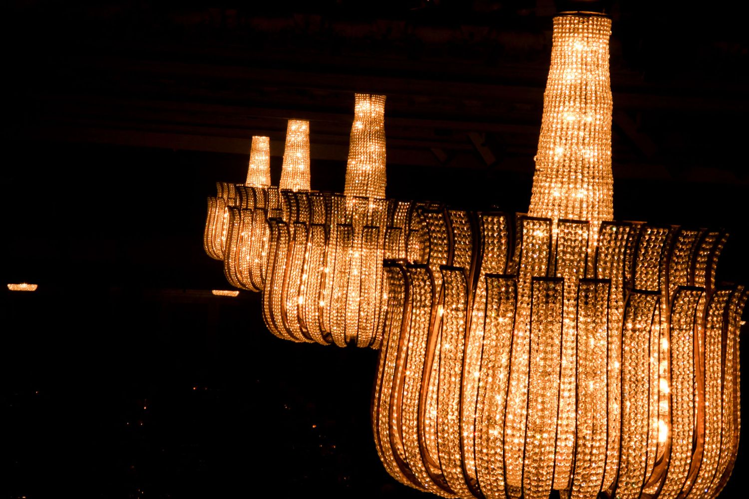 Crystal chandeliers create warm glowing patterns against dark background in elegant setting.