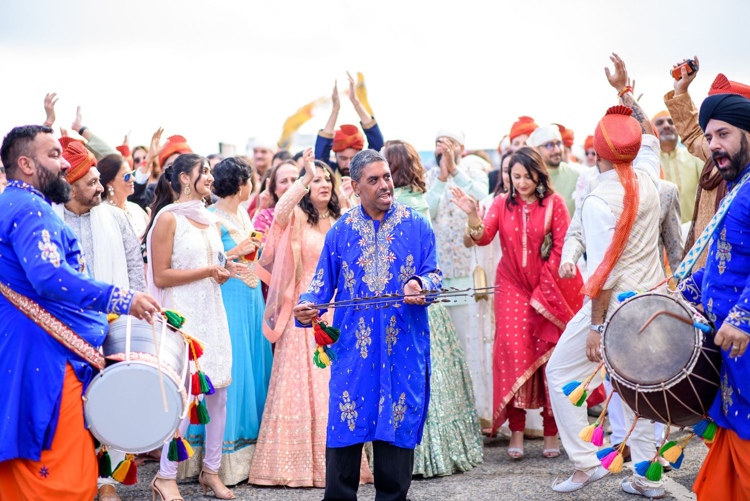A group of wedding guests in colorful traditional Indian attire dance and celebrate during a festive reception.