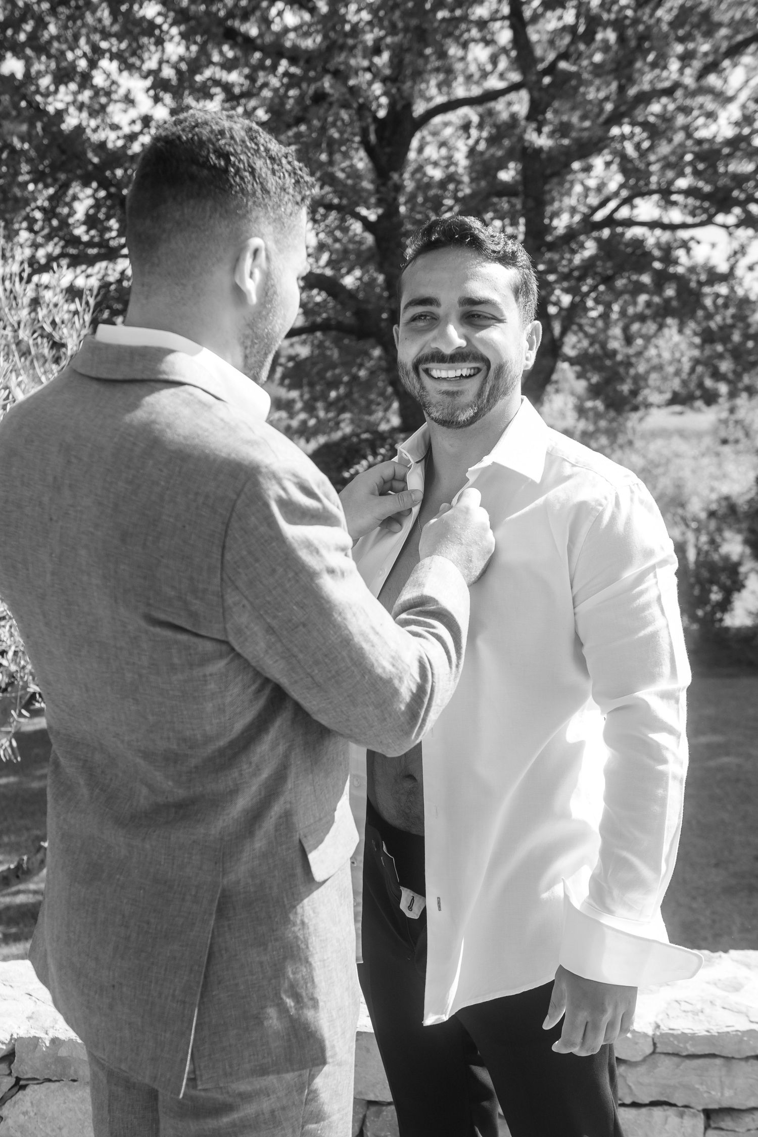 Two people share a joyful moment outdoors in black and white, one adjusting the other's tie.