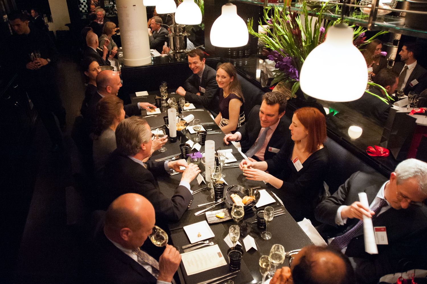 Diners seated at tables in a darkly lit upscale restaurant setting.