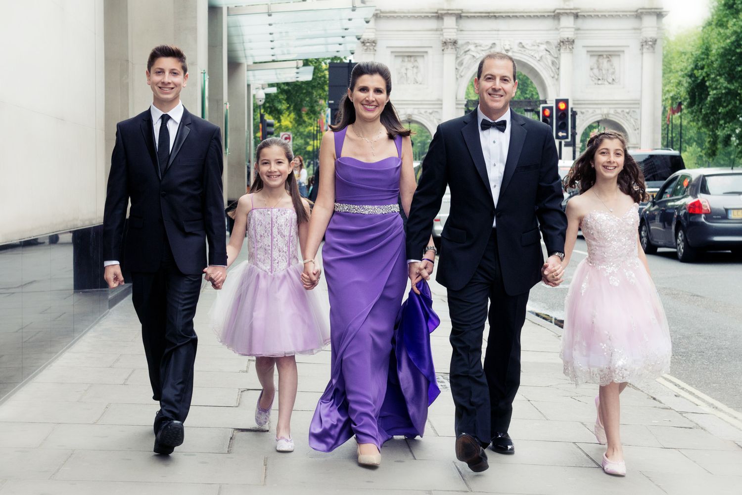 Wedding party members walk together wearing formal attire in purple and black with flower girls in pink dresses.