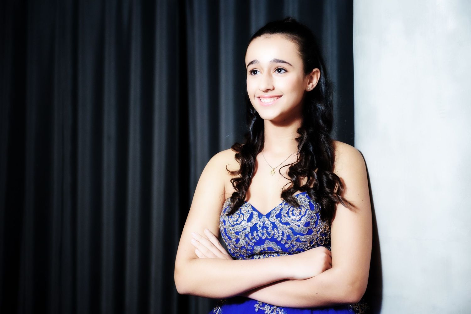 Young performer in a sparkling blue dress poses confidently against a white backdrop.