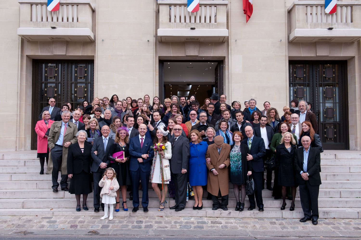 Large group of wedding guests pose for a panoramic photo on white stone steps of a building.