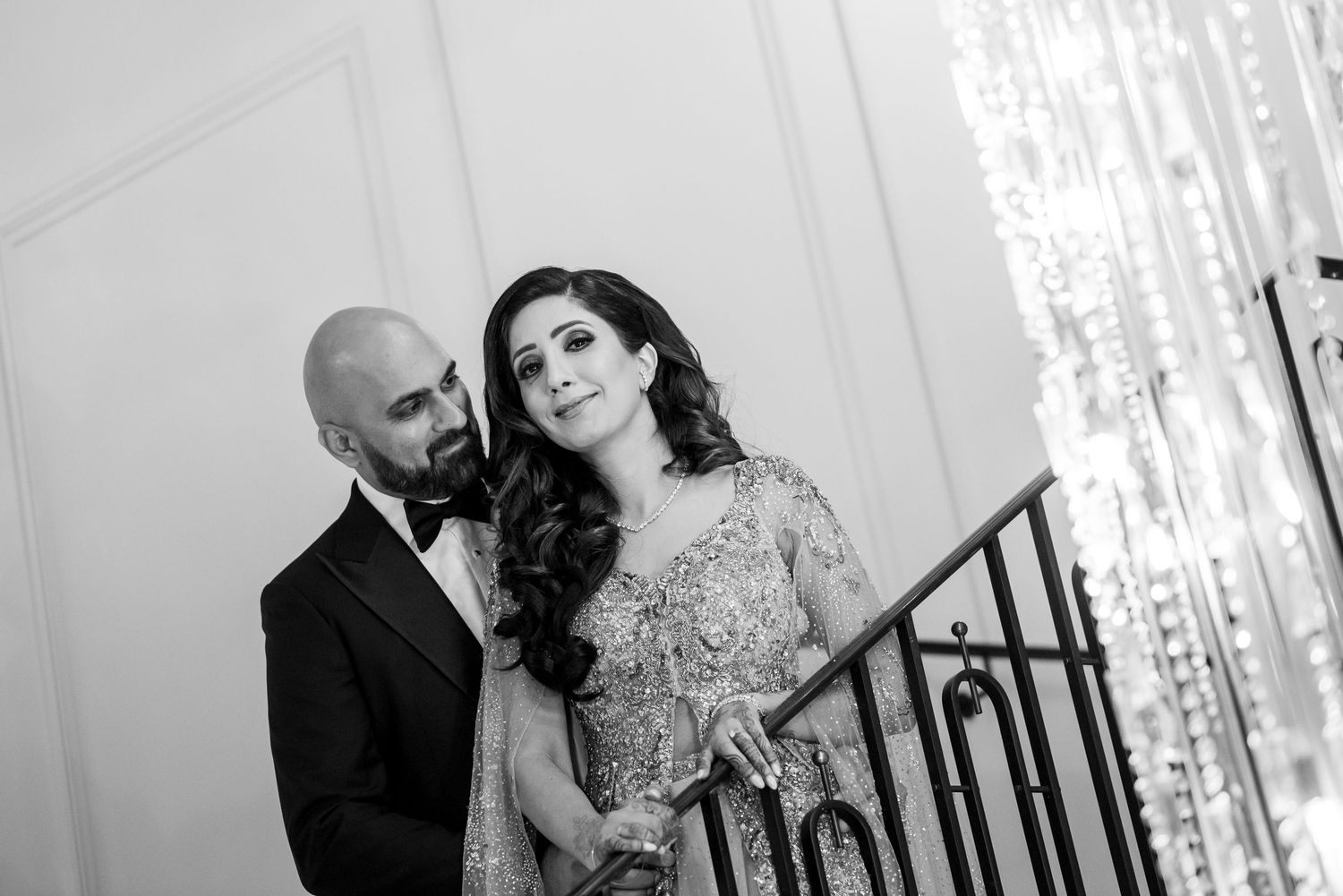 Elegant couple in formal attire pose together on a staircase in black and white photography.