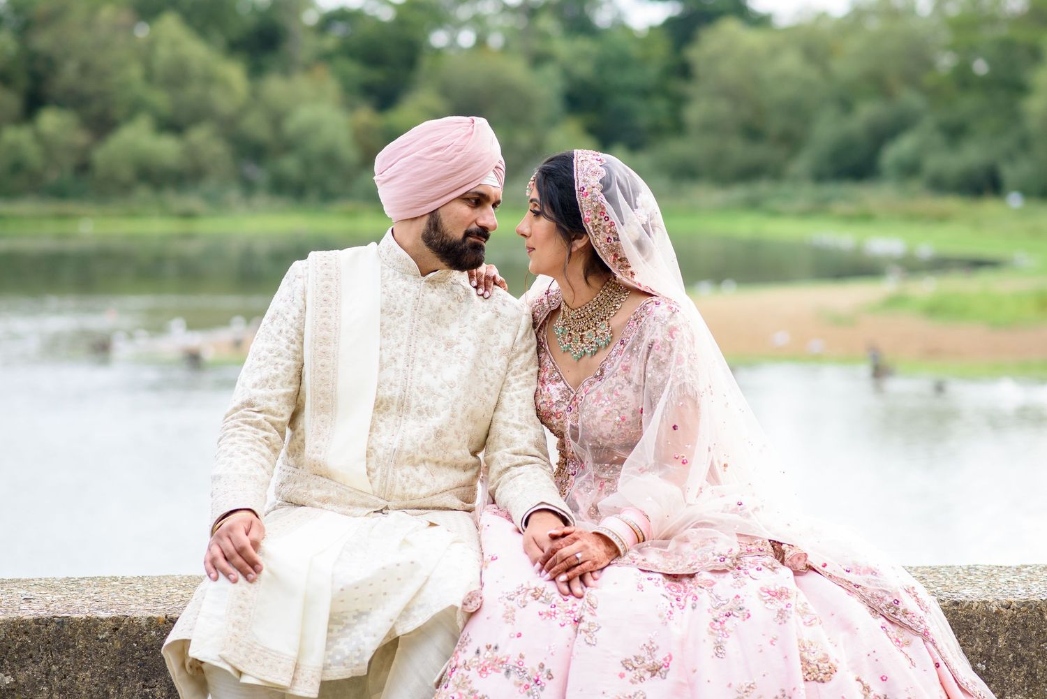 A couple in traditional Indian attire poses together by a lake during their wedding photoshoot.