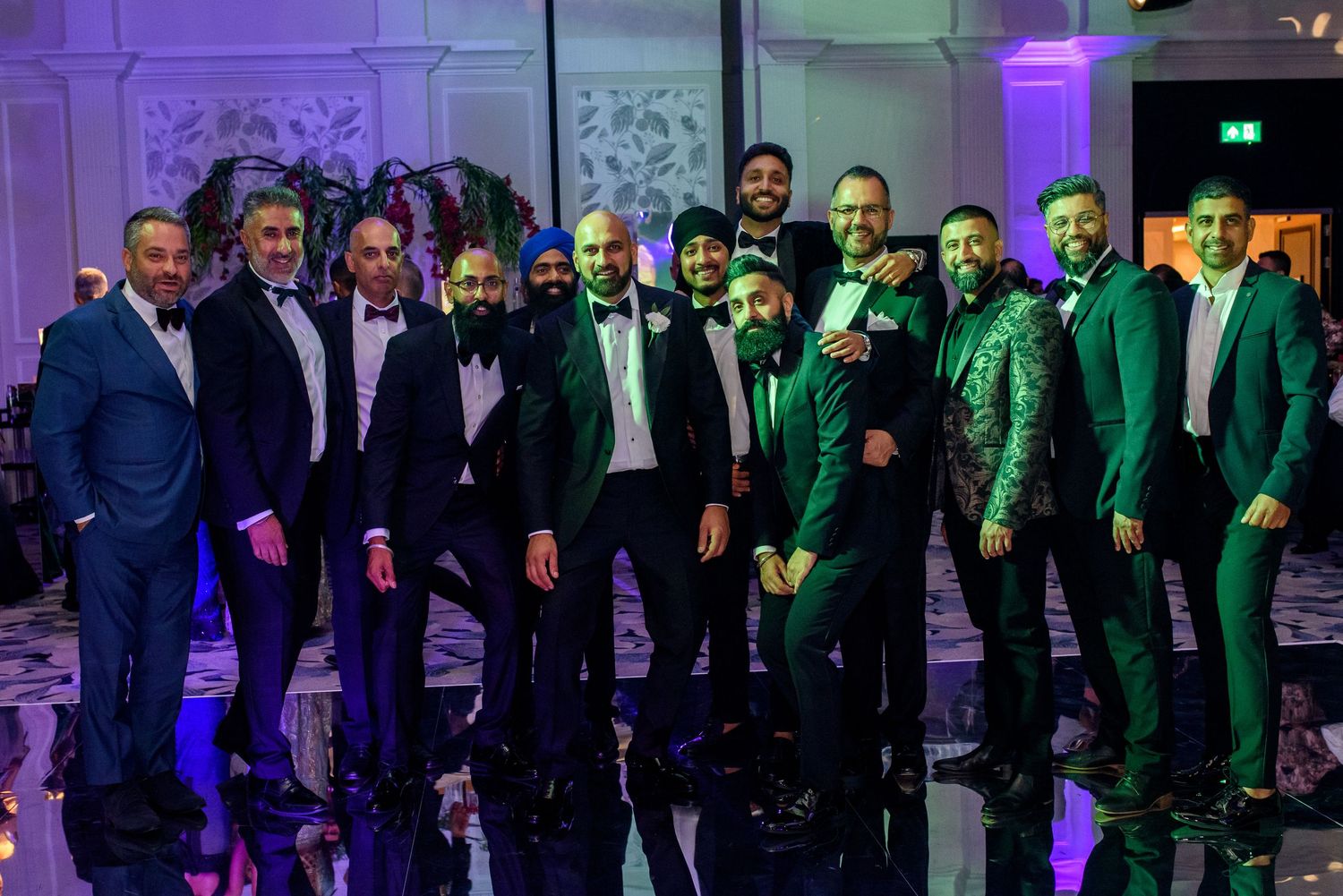 A group of formally dressed people standing in a line at an event with purple and green lighting effects.
