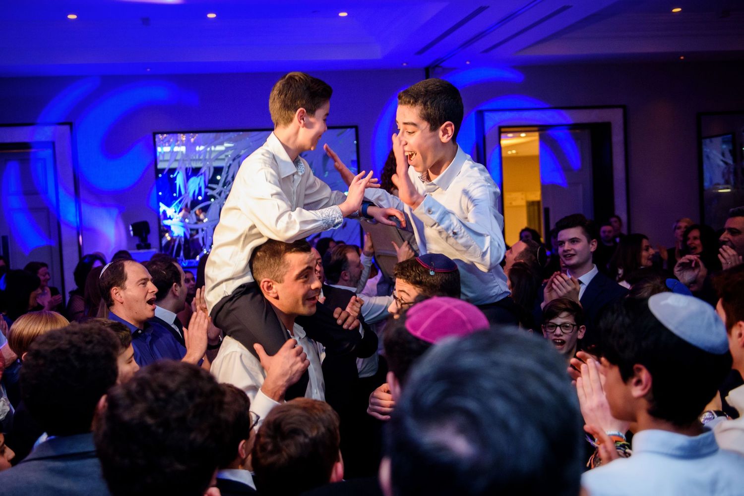 Energetic crowd at a concert venue with blue lighting as performers get carried by audience members during an enthusiastic show.