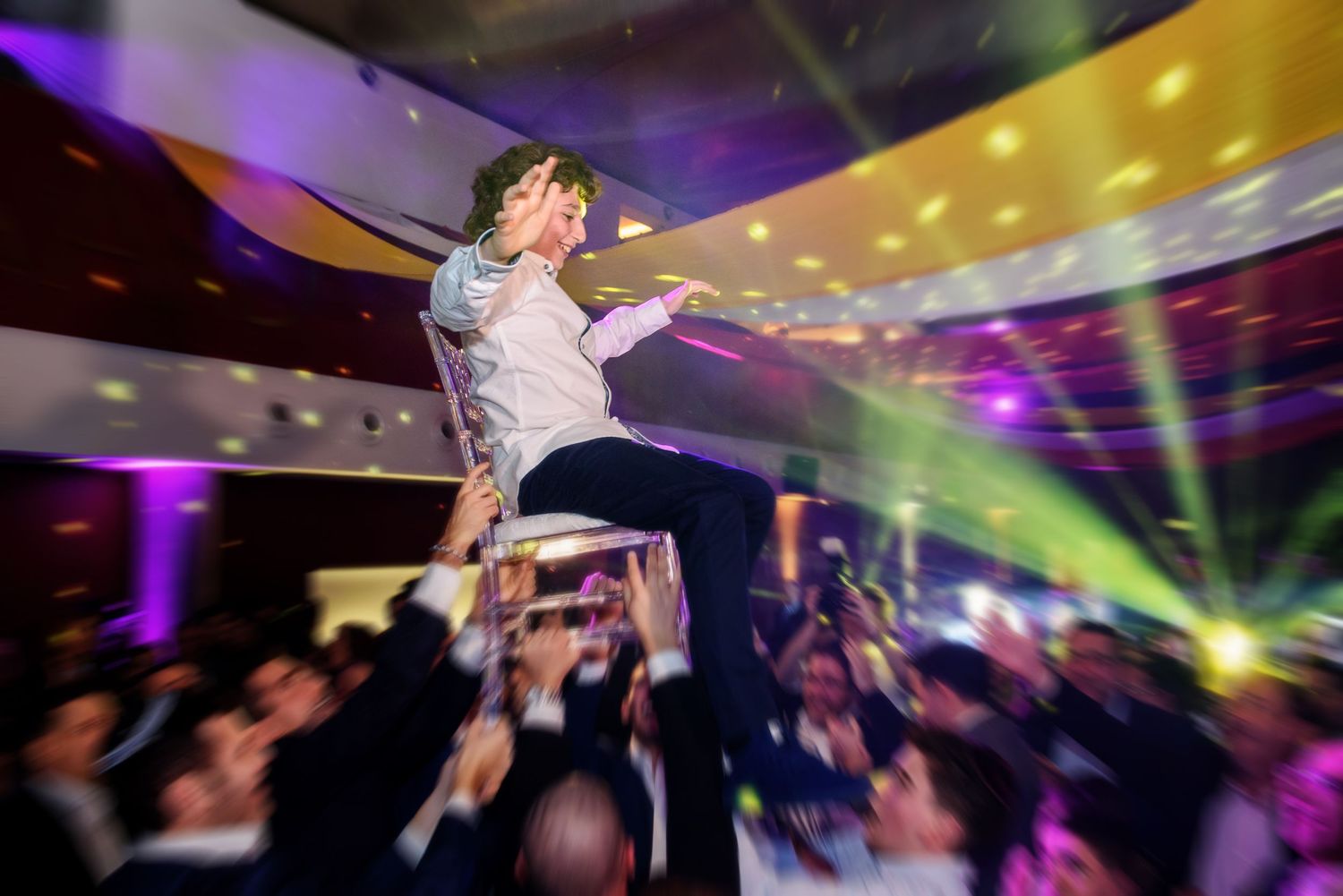 A crowd of people dancing and jumping at a nightclub with colorful purple and yellow lighting effects.