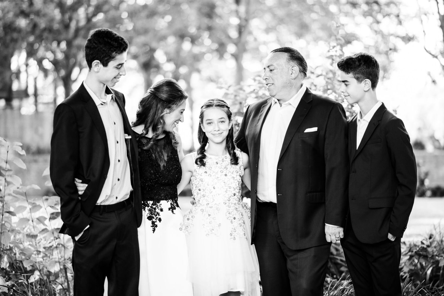 A wedding party in formal attire stands together outdoors in a black and white candid photograph.