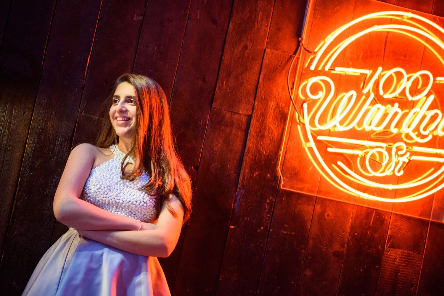 A person poses in front of a red neon sign against a dark wooden wall background.