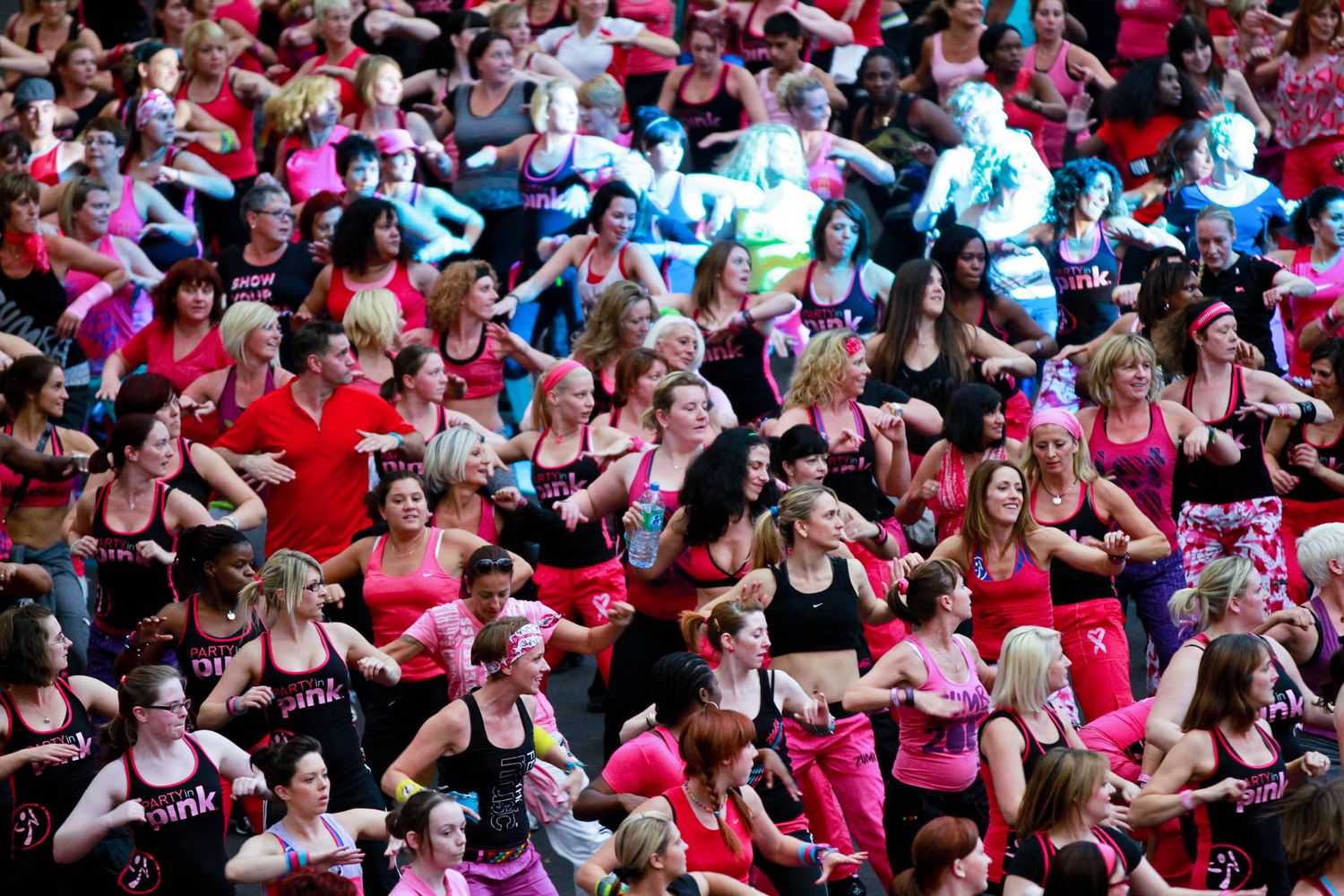 Large crowd wearing pink and red attire gathered at an outdoor event.