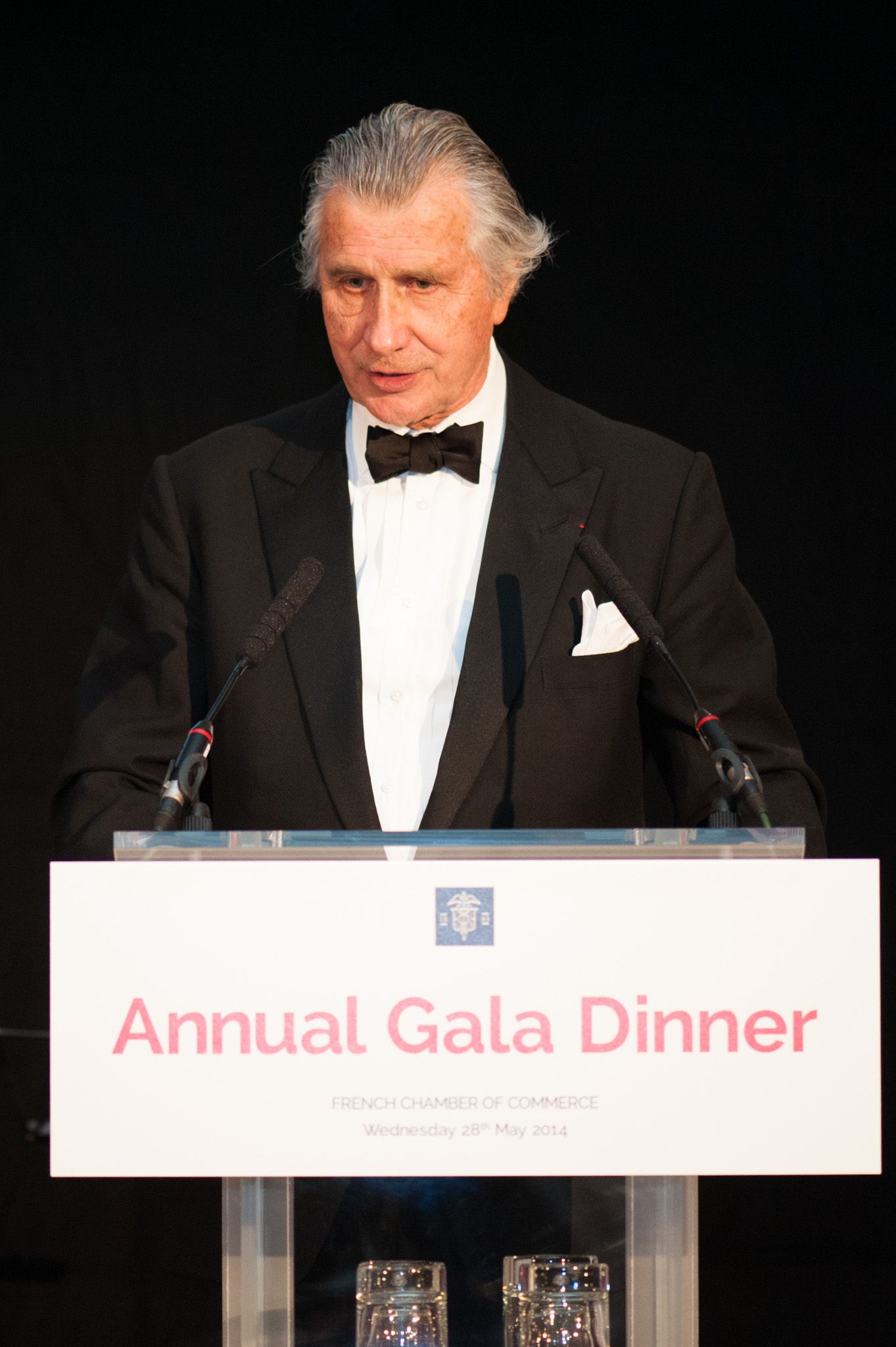 Speaker at formal gala dinner podium wearing black tie attire.