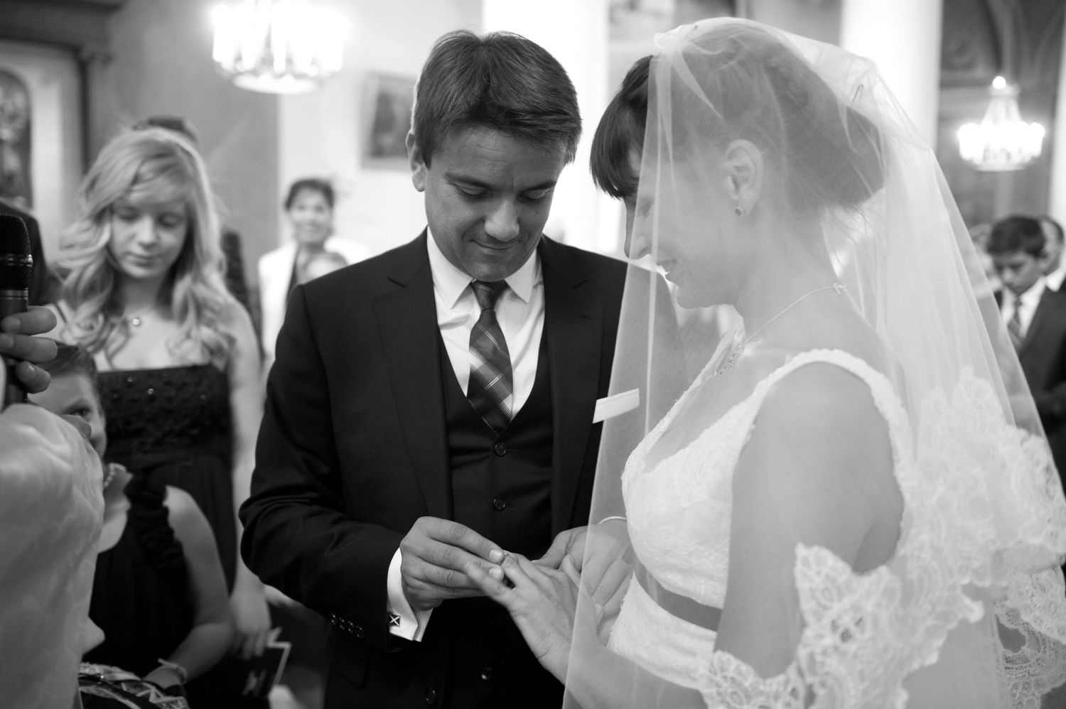 Groom placing wedding ring on brides finger during church ceremony in black and white photo.