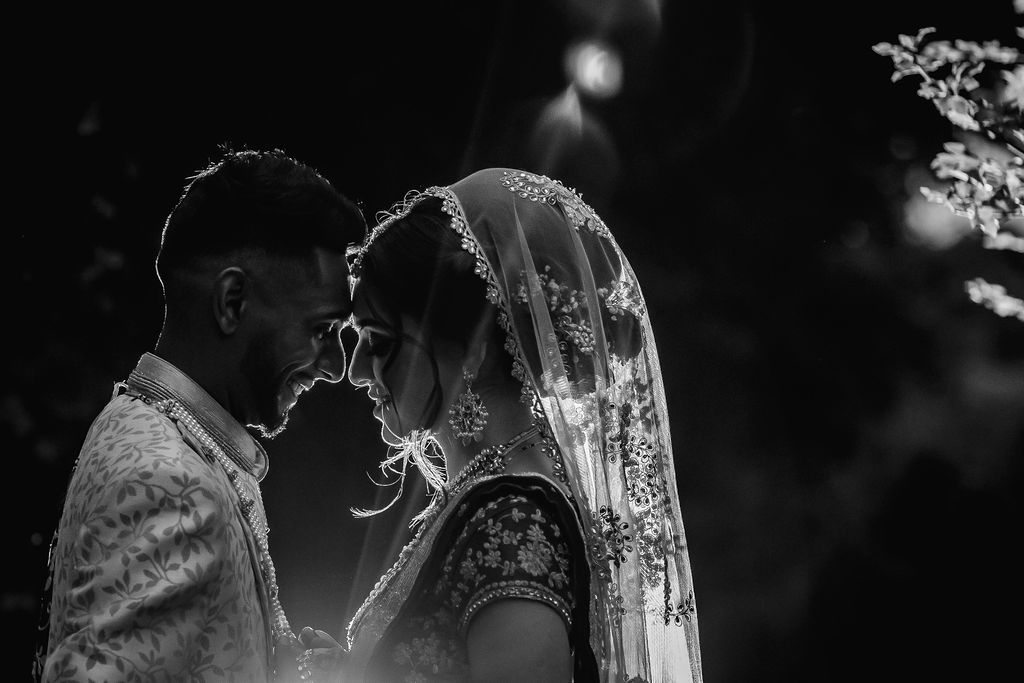 Black and white photo of an Indian bride and groom in traditional attire sharing an intimate moment at their wedding.