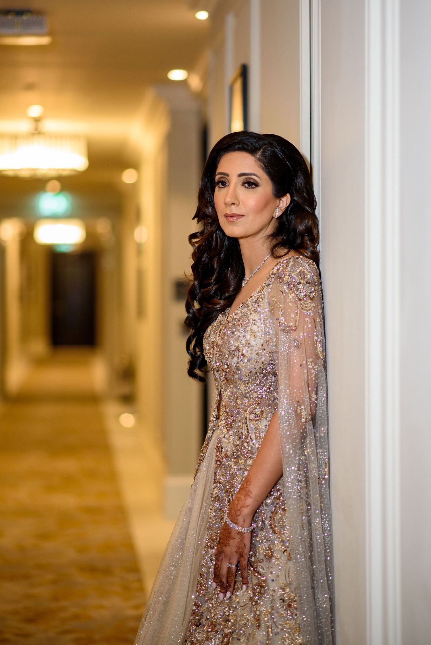 Elegant evening gown with intricate beading and sheer cape details photographed in a luxurious hotel hallway.