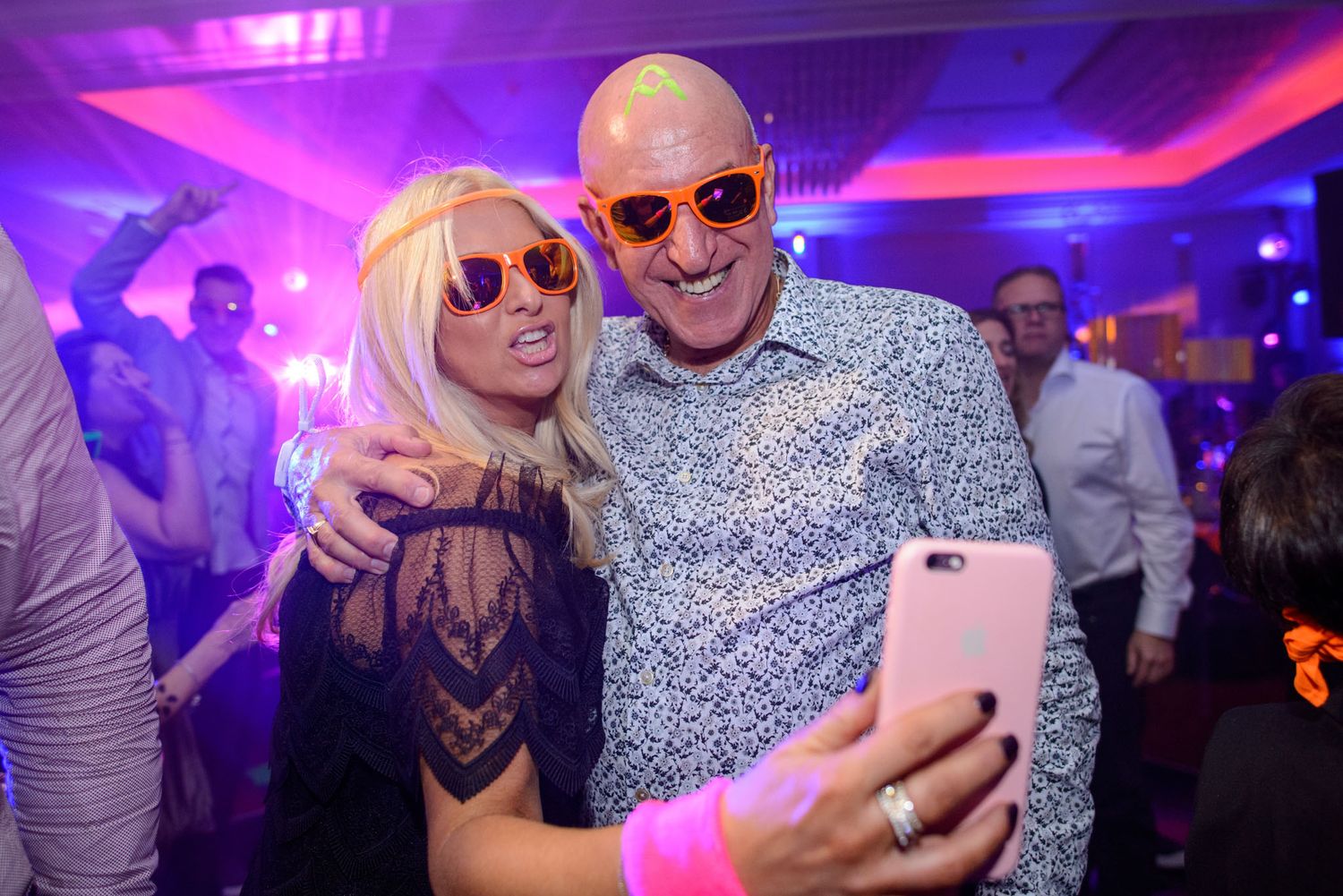 People enjoying themselves at a nightclub with purple lighting and taking selfies on the dance floor.
