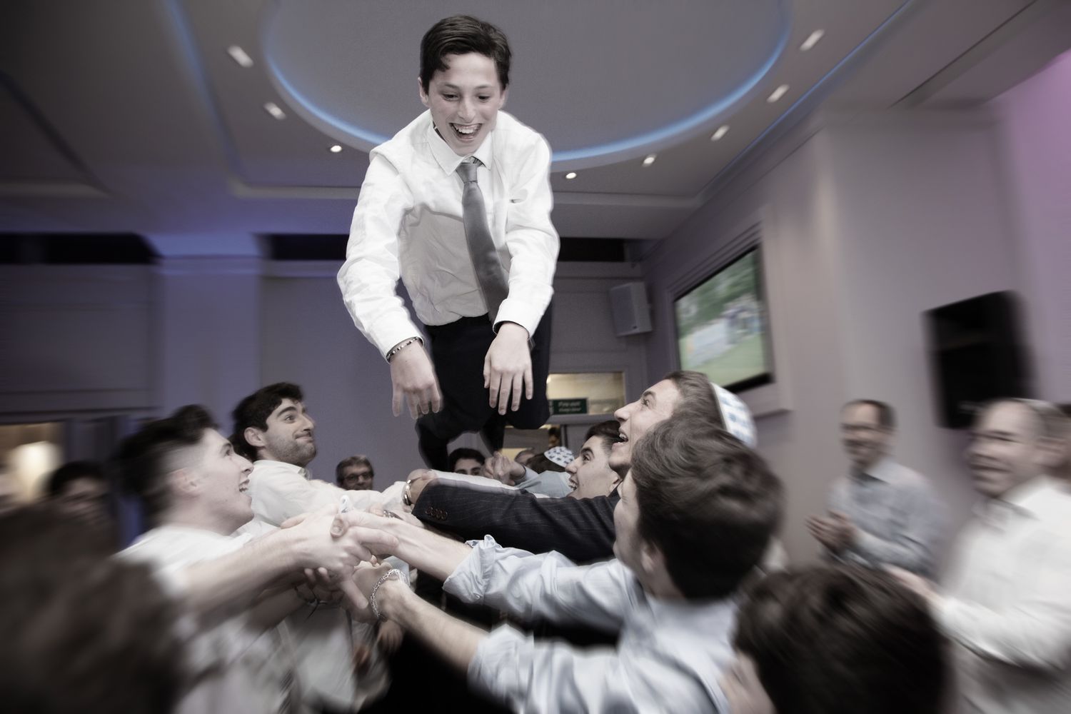 A celebratory scene shows someone being lifted up by a crowd during a festive indoor gathering.