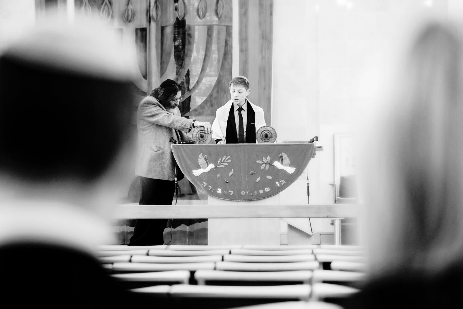 Rabbi leading prayer service in synagogue with traditional prayer shawl and tefillin.