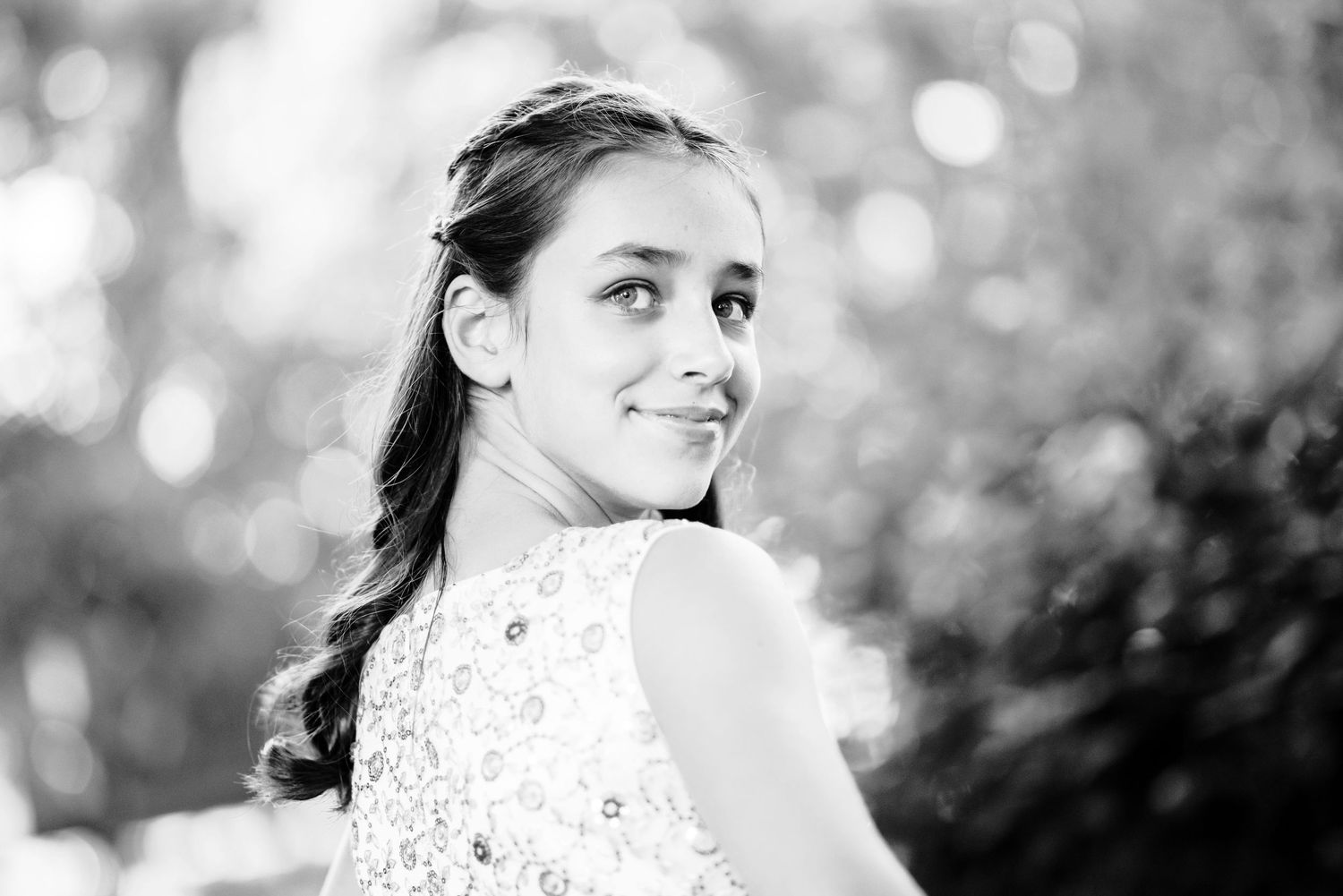 Black and white portrait of a young person wearing a lace top in an outdoor setting with soft bokeh lighting effects.