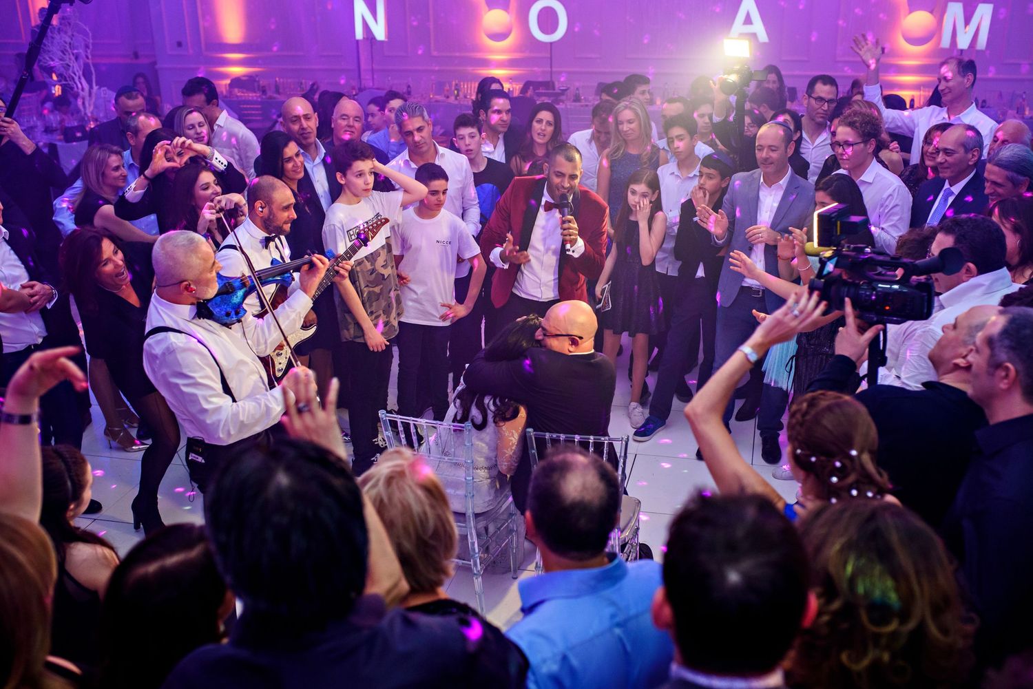 A crowded nightclub dance floor with people dancing under purple lighting and disco effects.