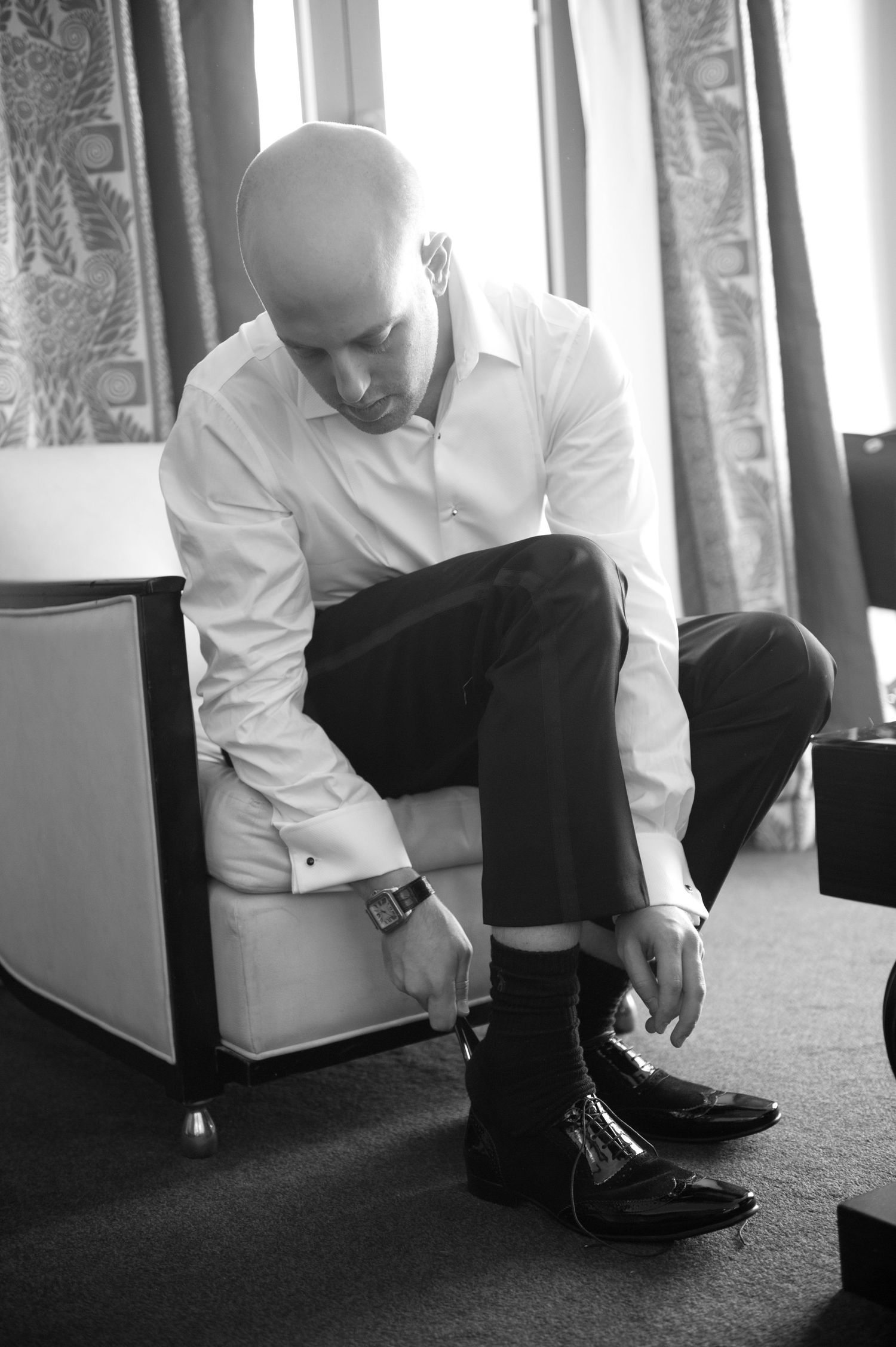 A sequence of black and white photos showing someone in formal attire tying dress shoes on carpet.