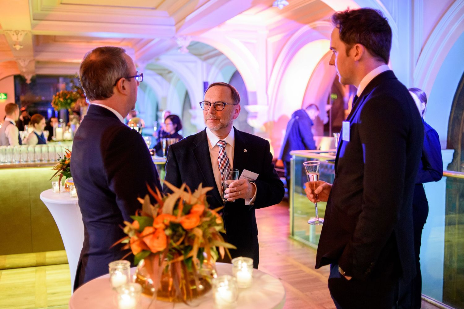 Business networking event in an elegant venue with purple lighting and floral centerpiece.