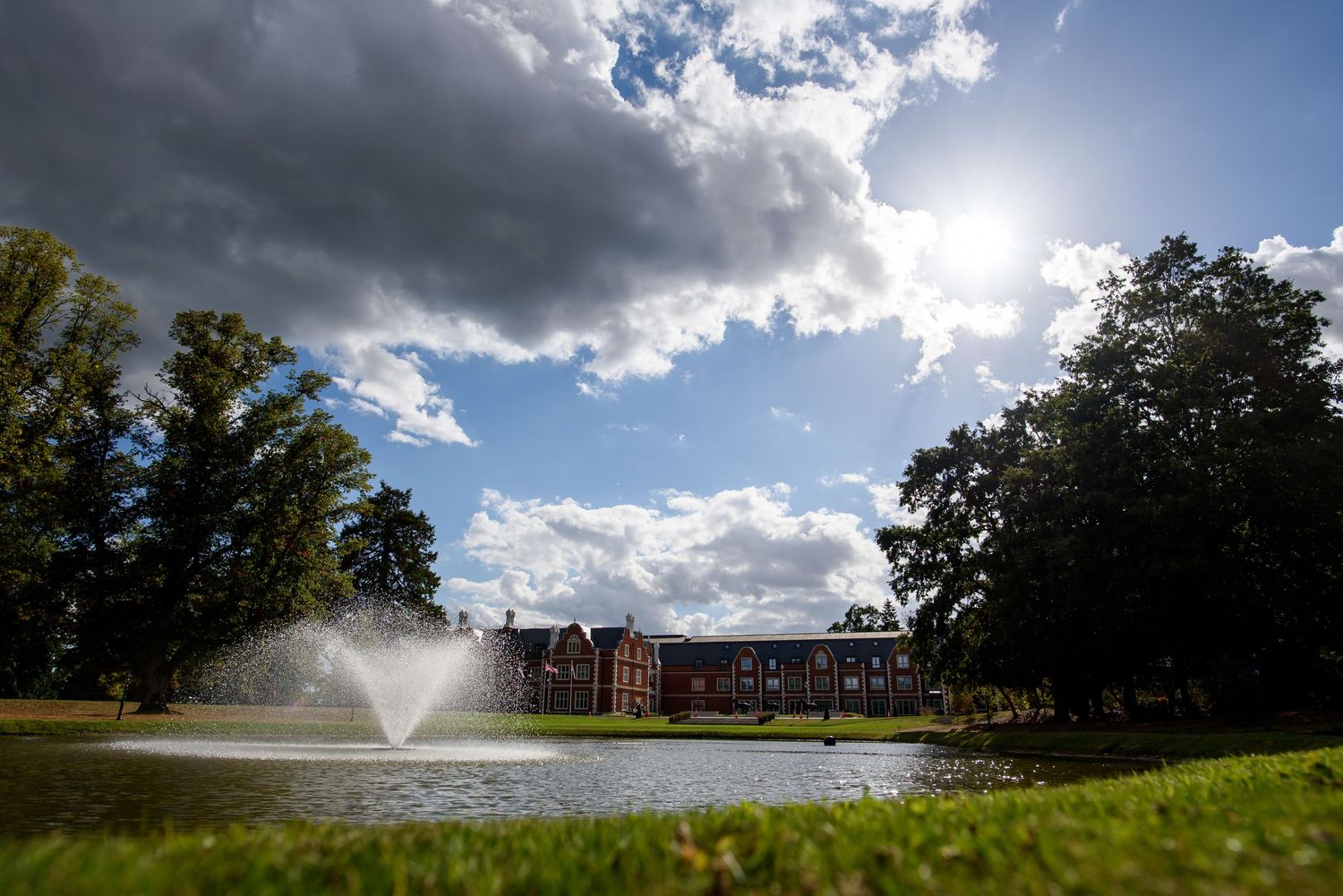 Dramatic panoramic view of a golf course landscape with water features and trees under a cloudy blue sky.