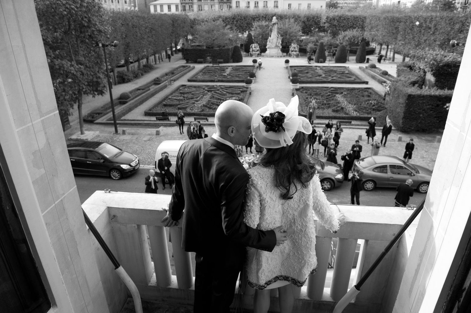 A black and white photo shows a line of people walking along a railing on a bridge or elevated walkway.