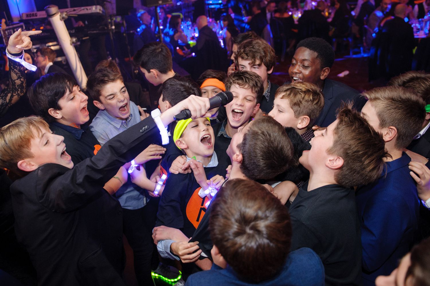 Energetic crowd of young people dancing and jumping at a concert with colorful lighting in the background.