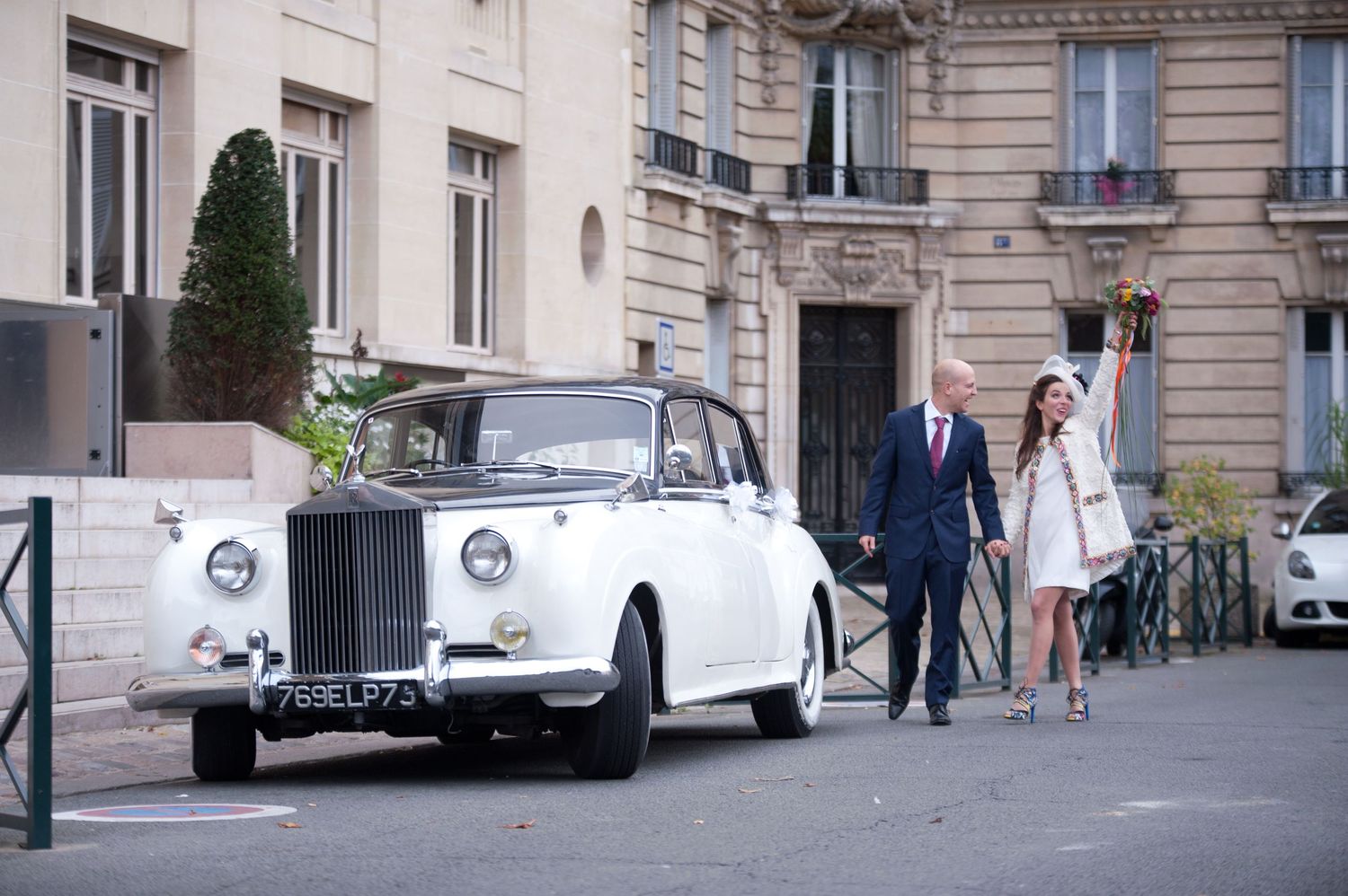 Vintage white Rolls-Royce wedding car parked outside elegant stone building with classic architecture details.