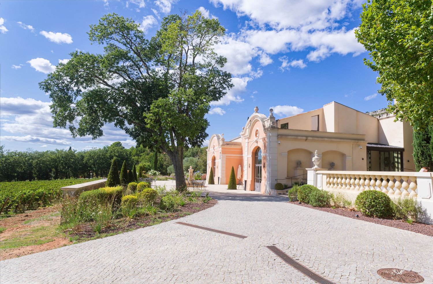 Elegant Mediterranean villa with arched entrance and white gravel driveway surrounded by manicured gardens and tall trees.