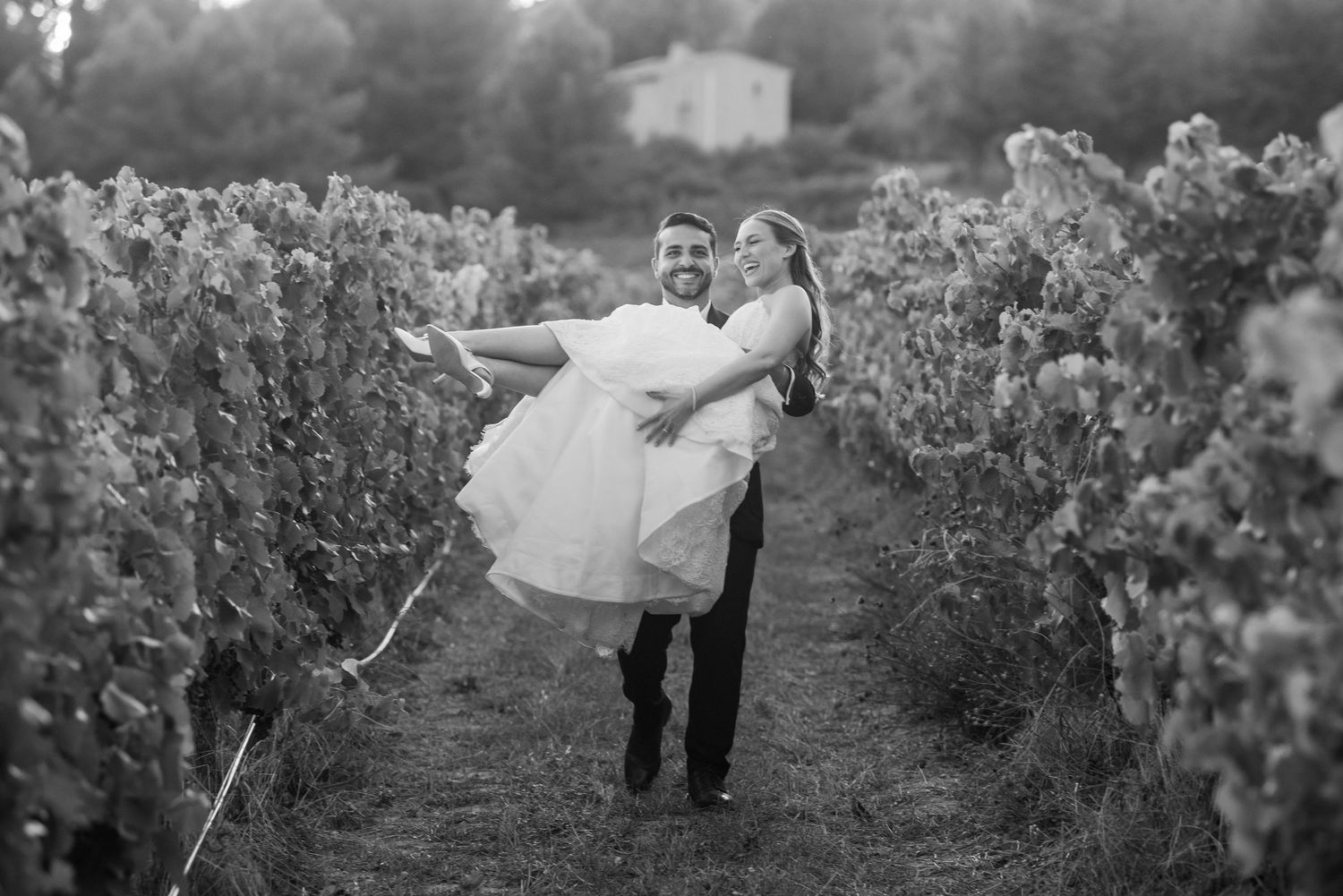 Black and white photograph of a couple dancing in a vineyard during a romantic sunset moment.