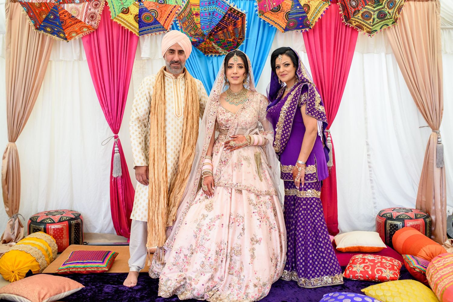 Colorful Indian wedding celebration with traditional outfits and decor featuring pink and gold draping.