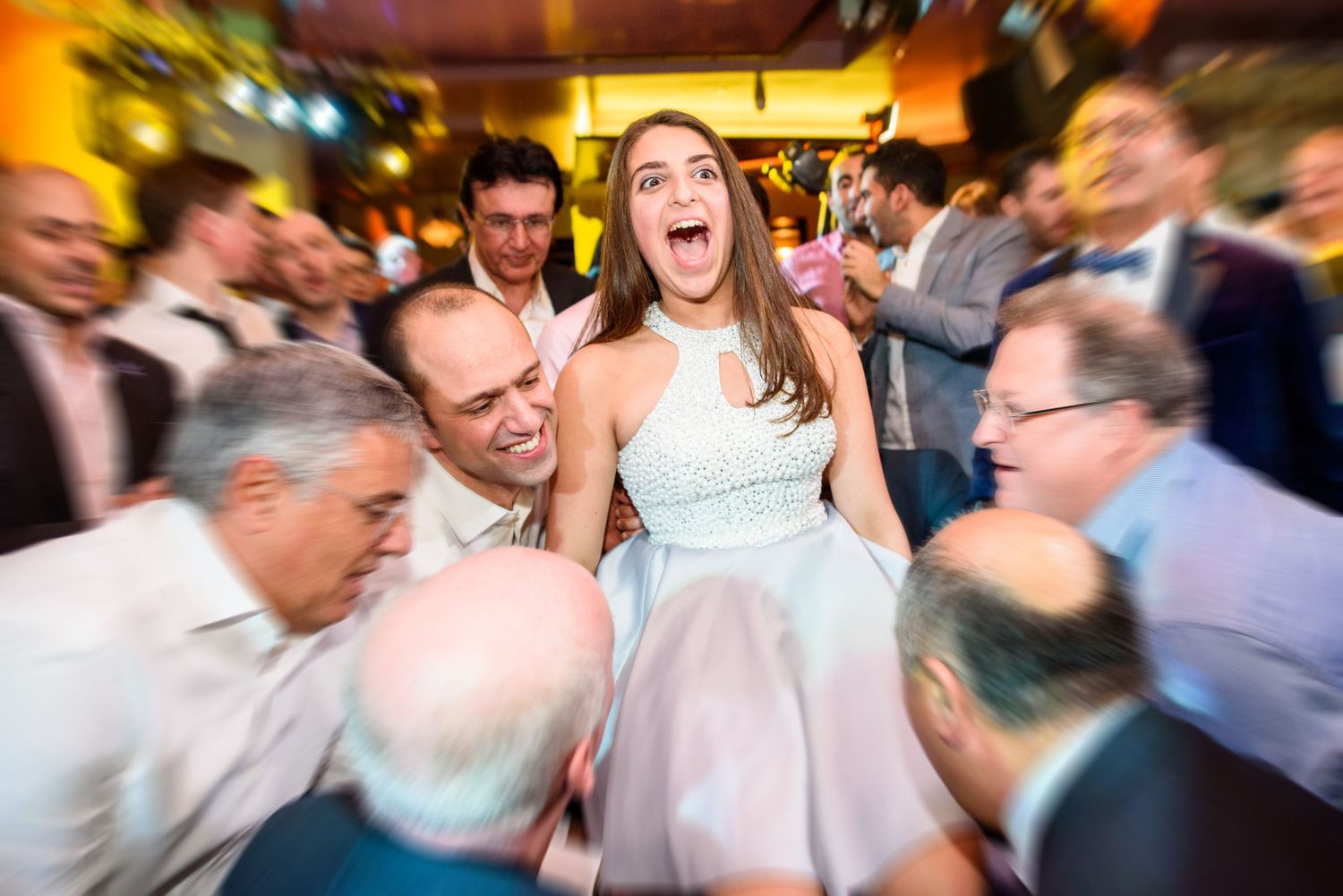 Energetic dance floor scene at wedding reception with motion-blurred guests celebrating.