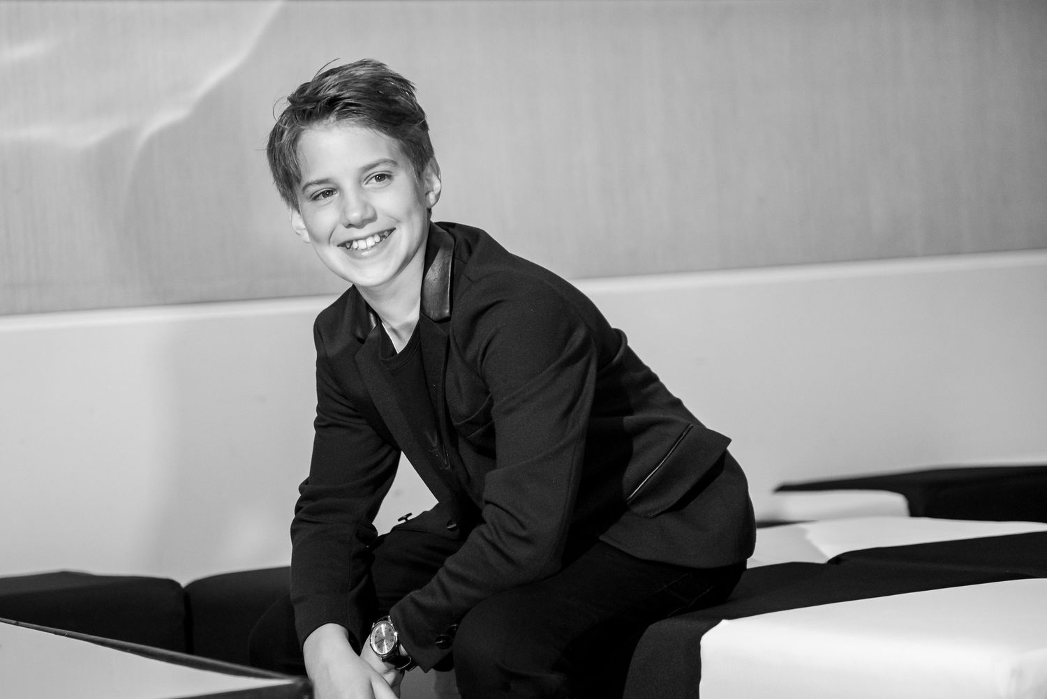 Black and white portrait of someone in casual attire sitting on a couch with a bright smile.