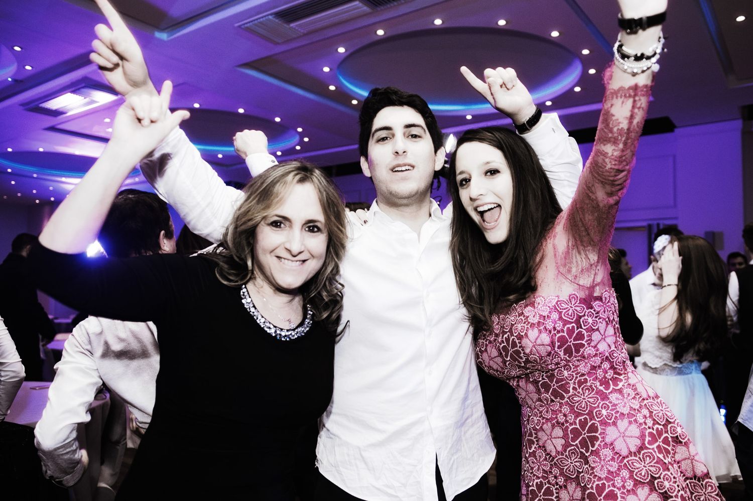 Wedding party dancing under purple mood lighting in an elegant reception venue.