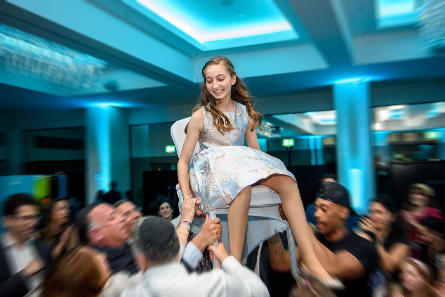 A bride in a white wedding dress dances with guests at a reception with blue lighting and decor.