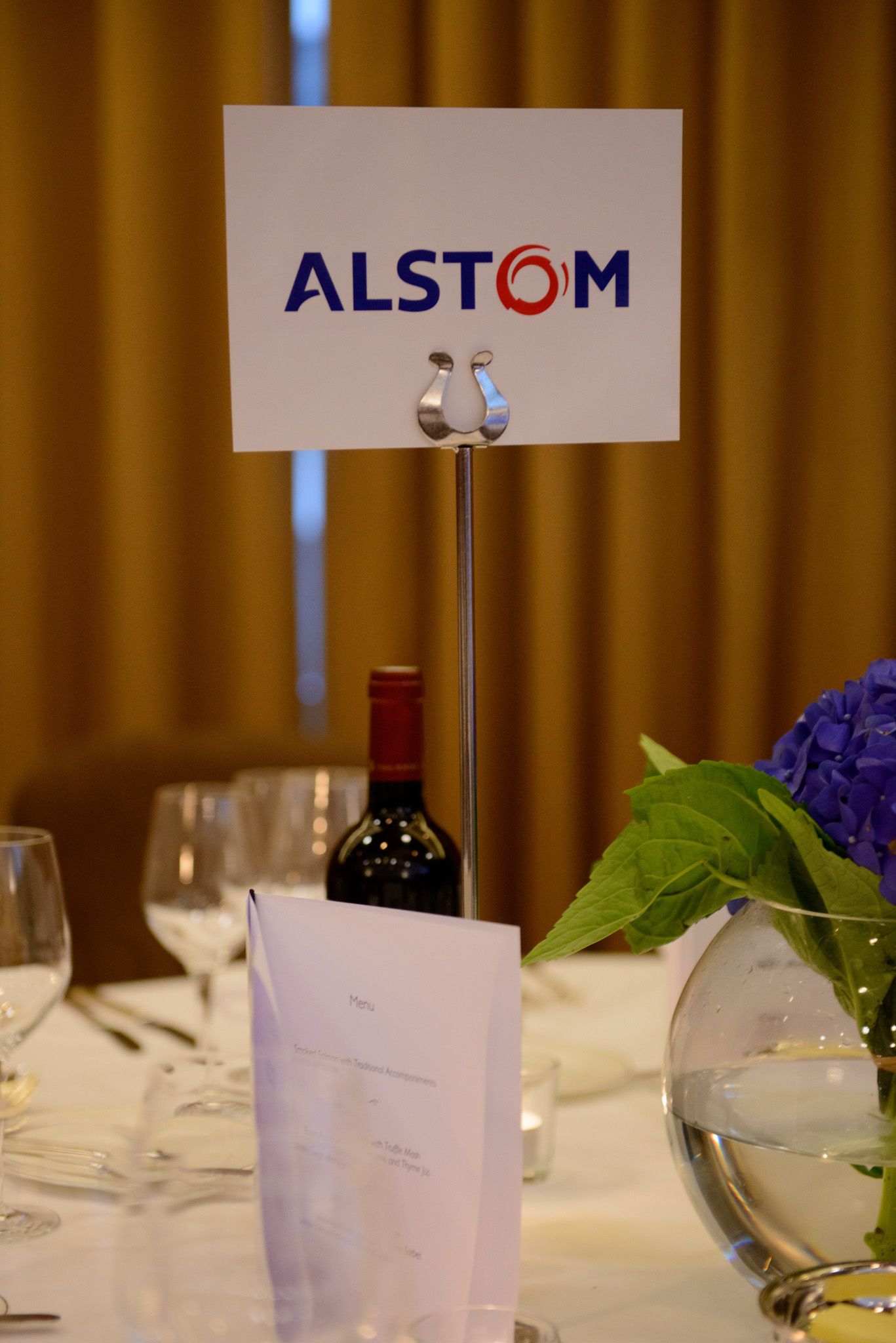 Elegant table setting with wine glasses and Alstom corporate signage at formal dinner event.
