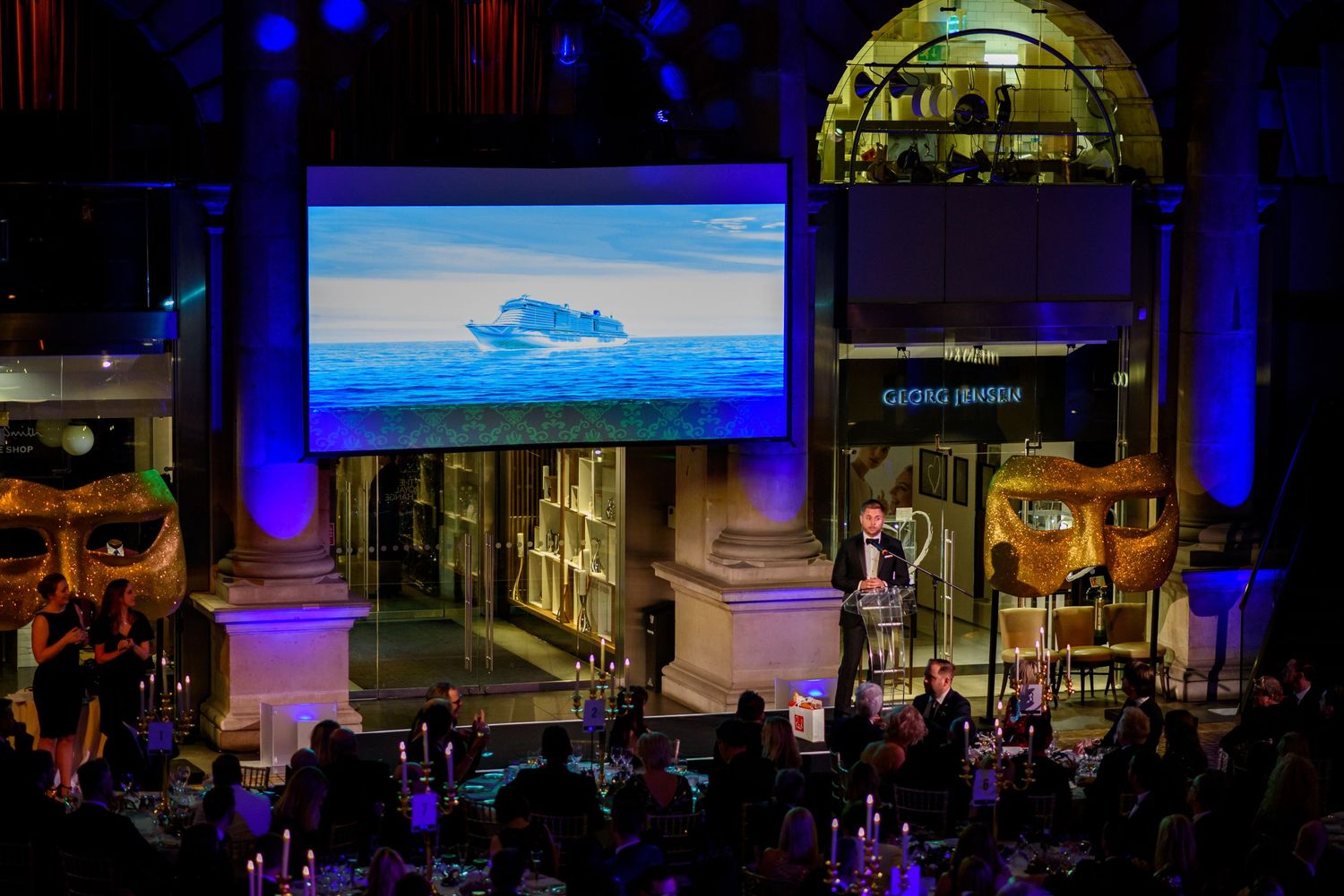 Event venue with dramatic blue lighting and projection screens displaying presentations during a corporate gathering.