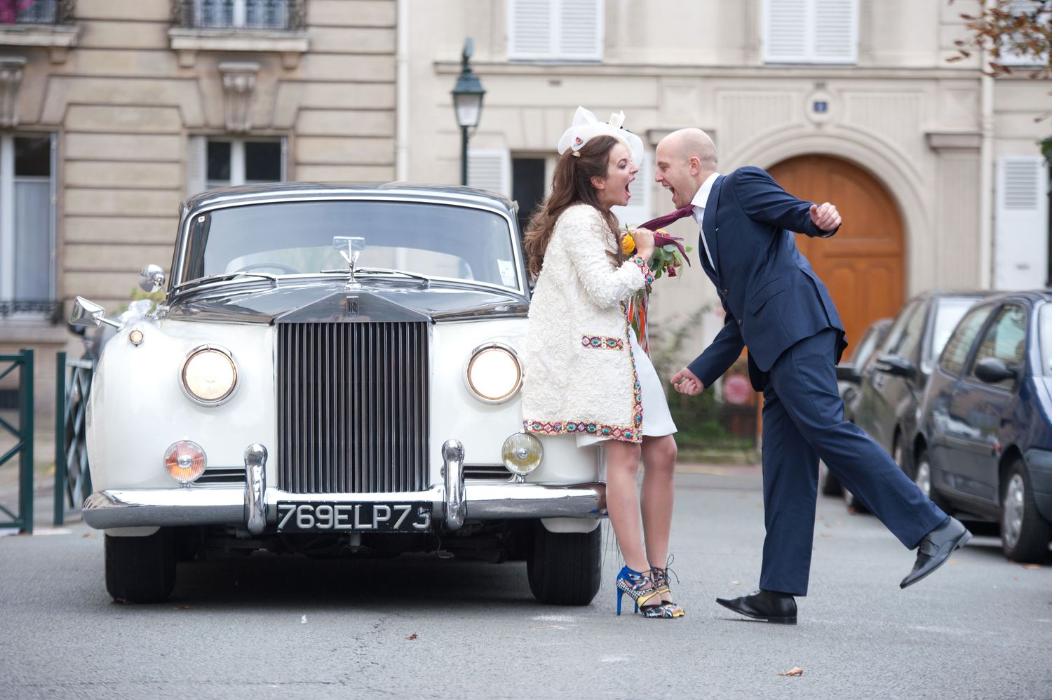 Vintage Rolls Royce cars parked in a row outside classic European buildings during a wedding celebration.