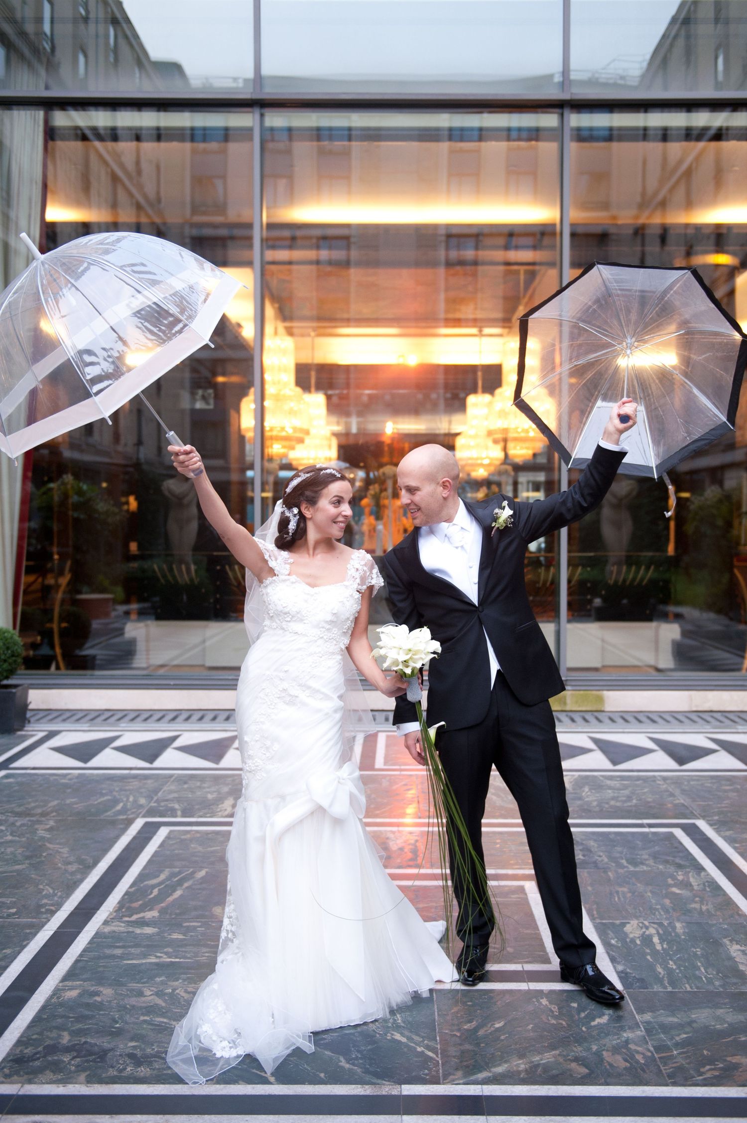 A couple shares a romantic dance with umbrellas in front of a modern building at twilight.