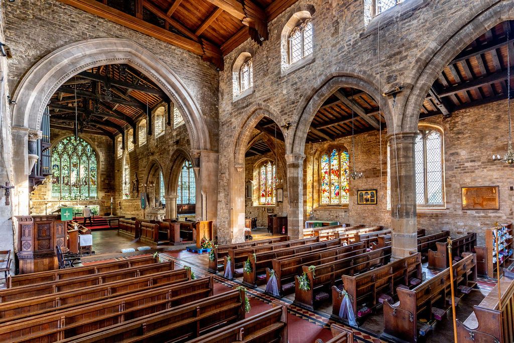 Interior of a historic stone church featuring wooden pews, arched columns, and vibrant stained glass windows.