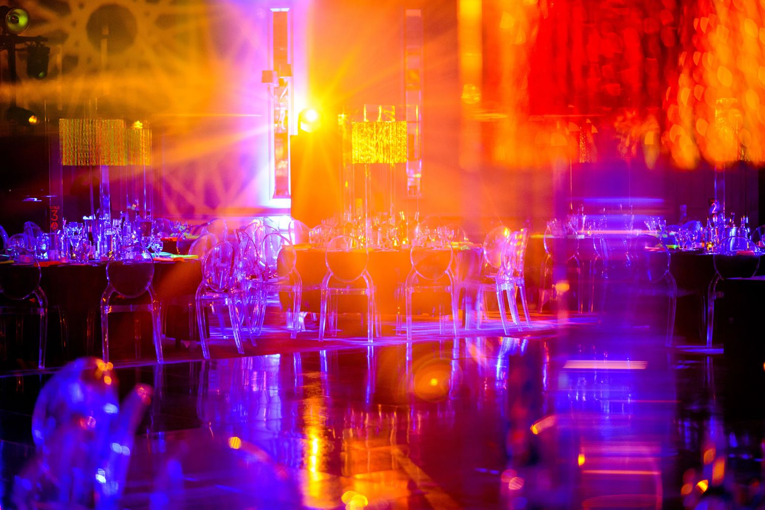 Vibrant purple and orange neon lights illuminate a nightclub interior with glowing reflections and atmospheric haze.