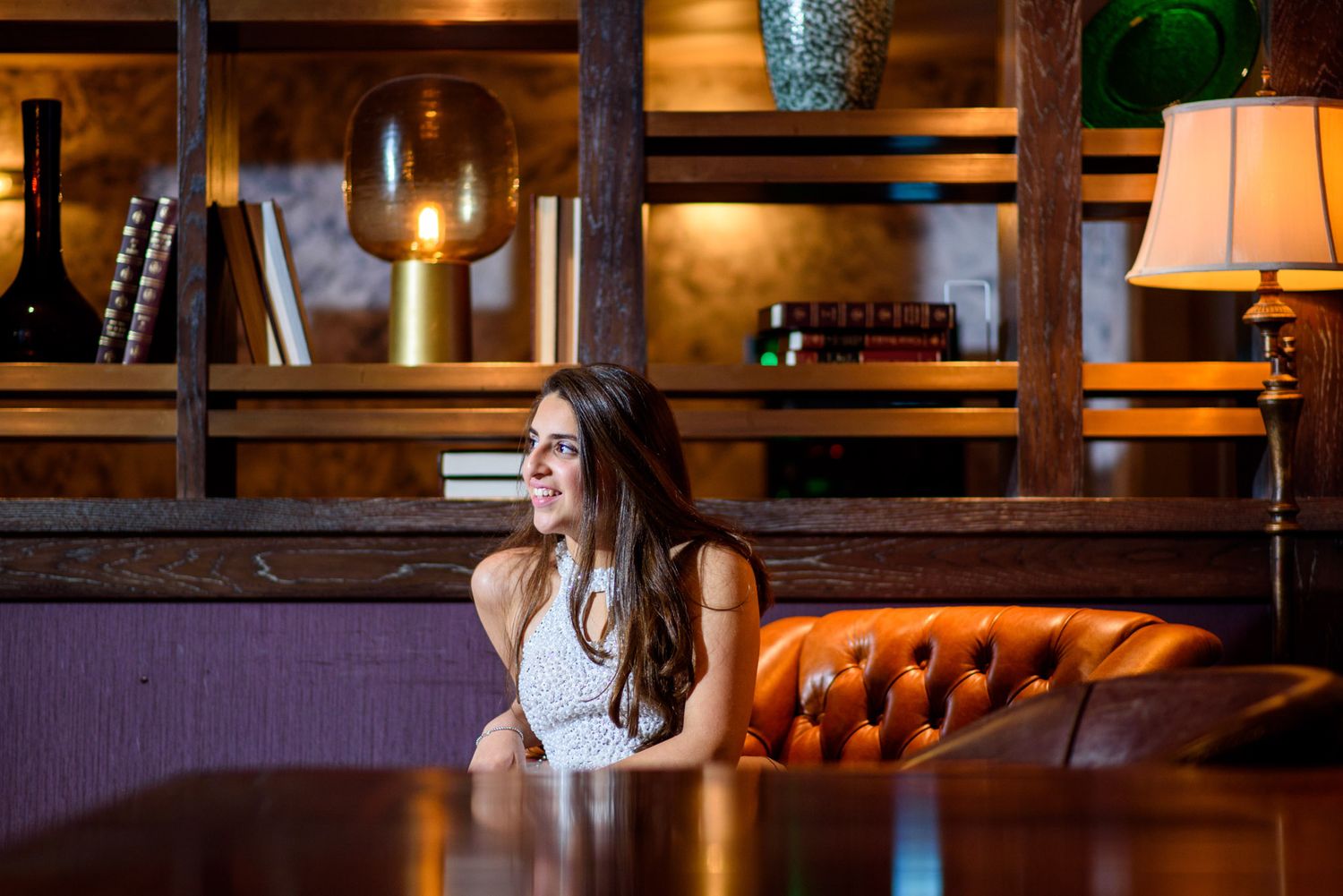 A cozy bar interior with warm lighting features leather tufted seating and wood paneling on the walls.