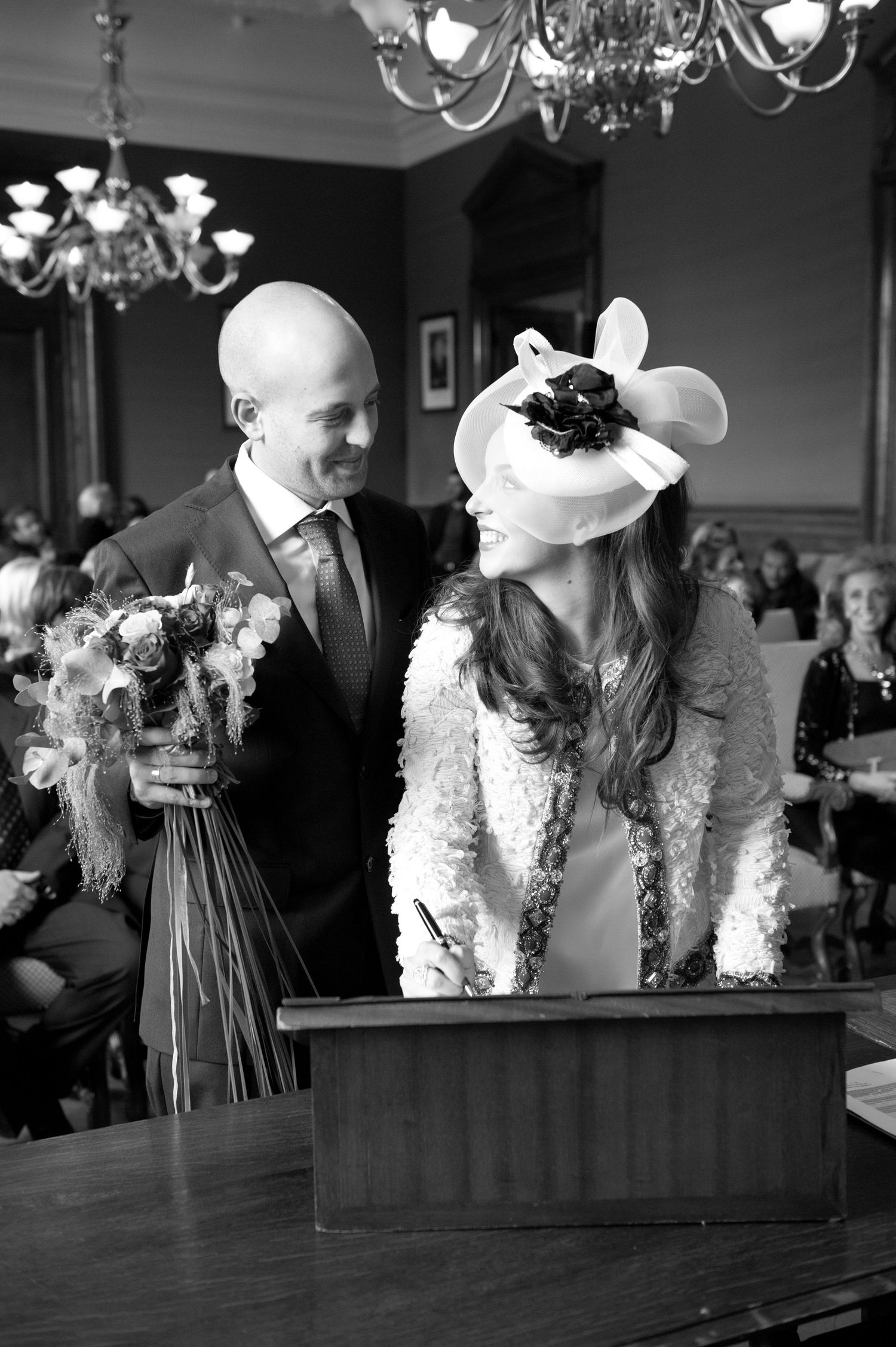 Black and white photo of wedding decor with feathered centerpieces and chandeliers in an elegant dining room.
