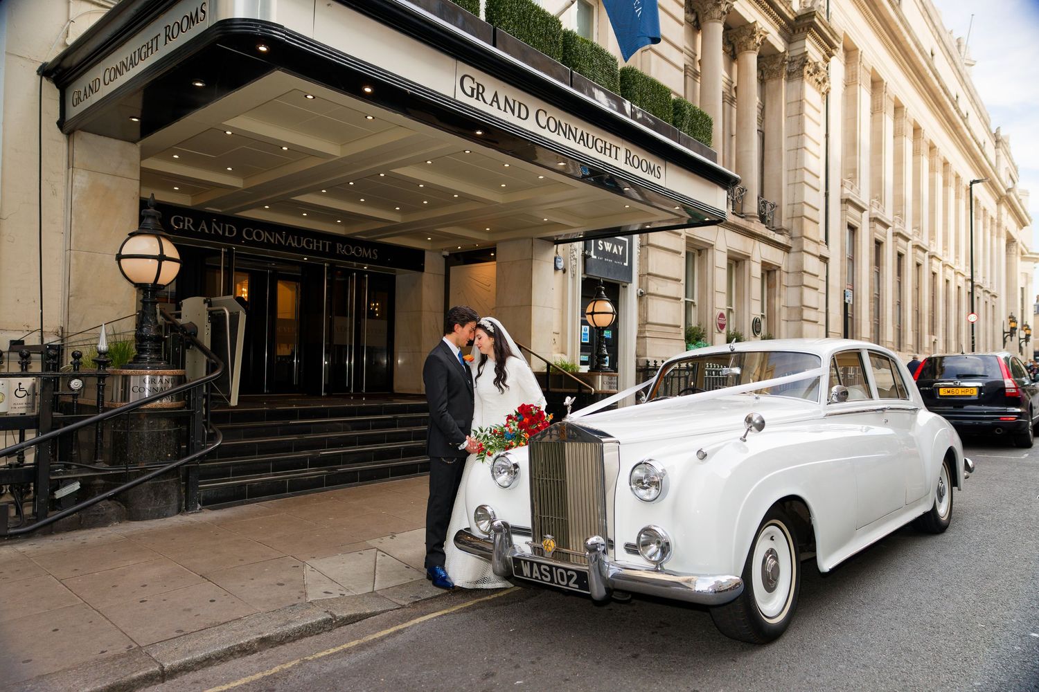A luxurious white vintage Rolls Royce wedding car parked on a European city street with classic architecture.