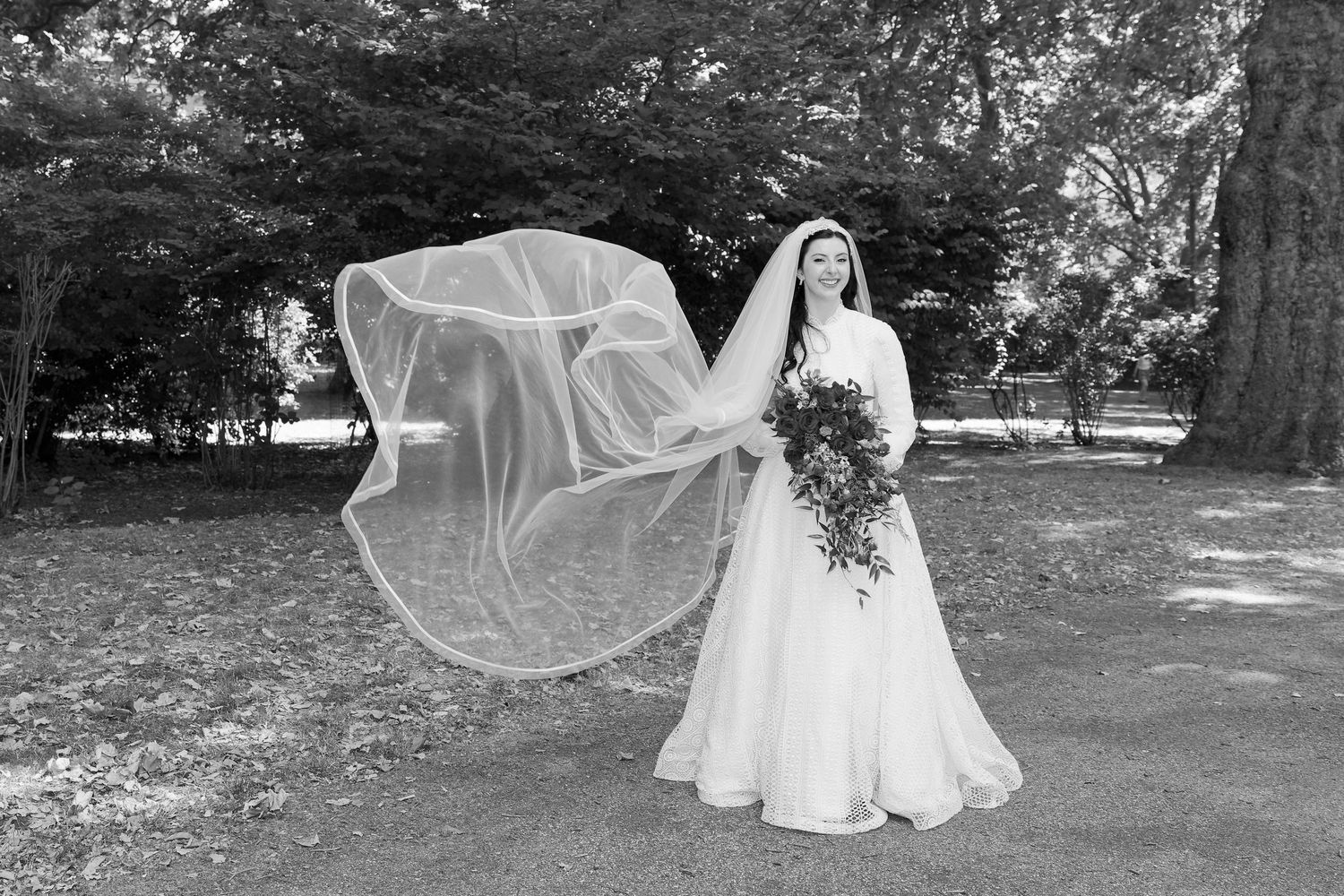 A flowing white wedding dress twirls gracefully in a sun-dappled outdoor garden setting.