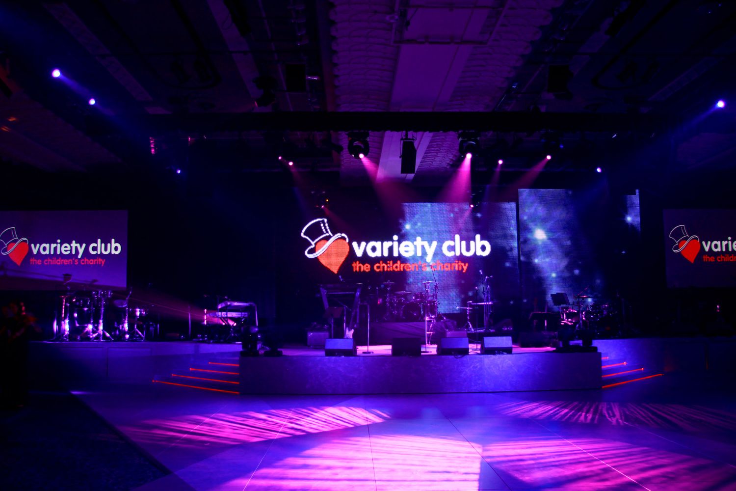 Purple-lit event space with Variety Club branding and stage lighting.