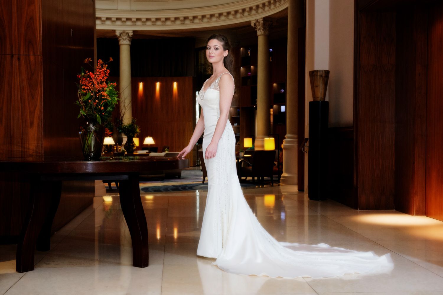 Elegant bride in a white fitted mermaid wedding gown with train poses in a luxurious hotel lobby.